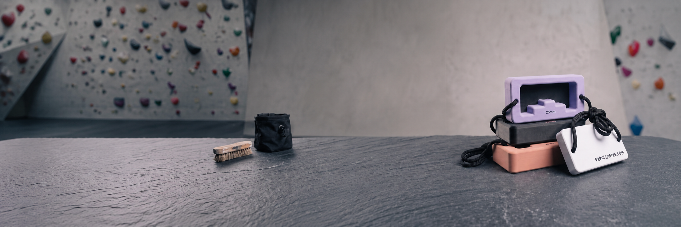 A stack of DAB climbing blocks on a gym bench beside a chalk bag and brush